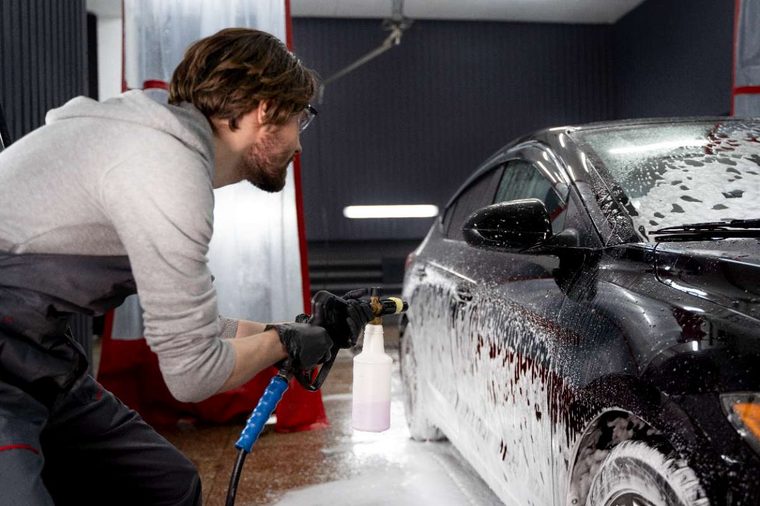 Detailer applying foam cannon wash to a black car
