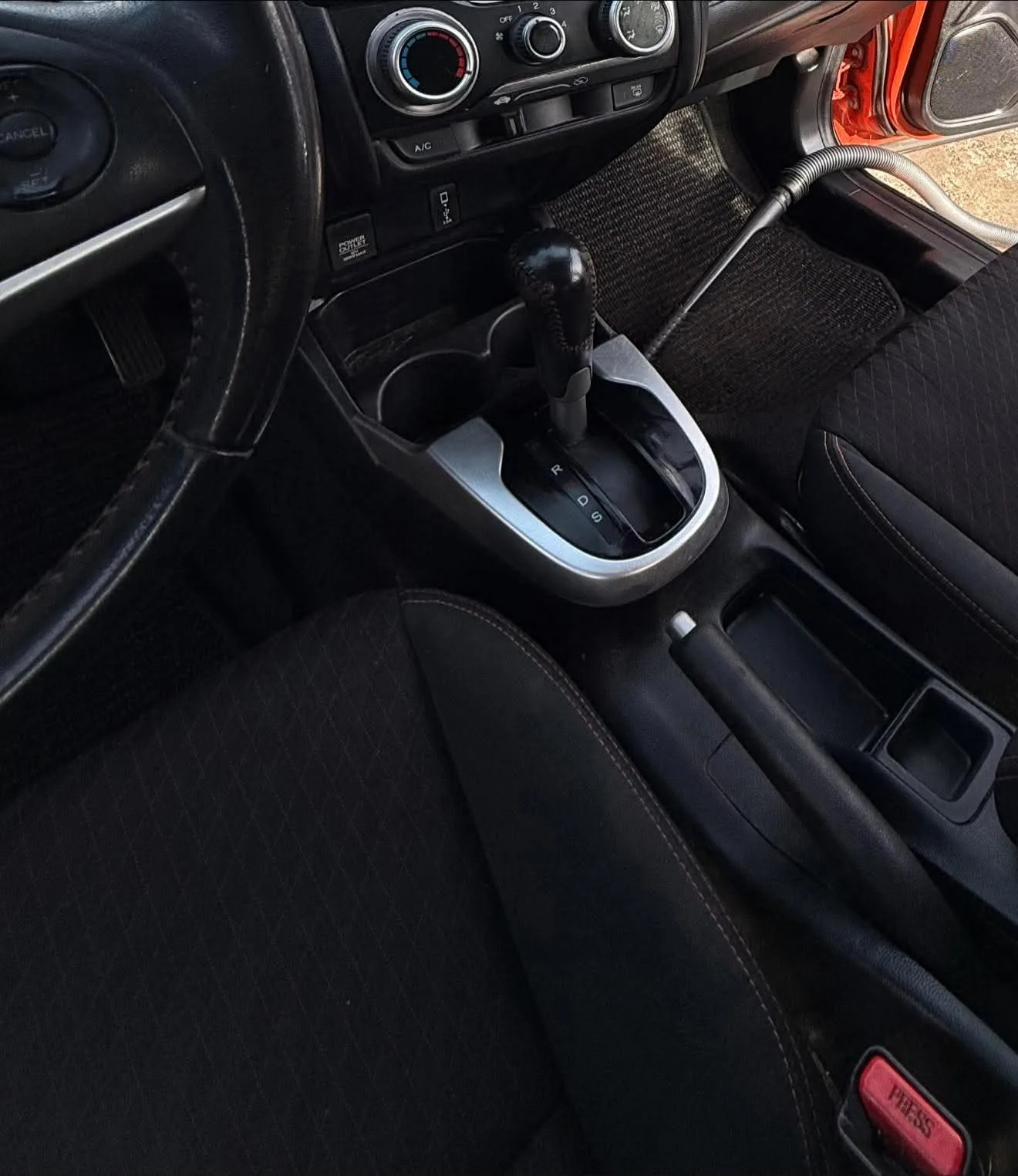 Foto real de la consola central y la palanca de cambios de un Honda rojo después del detallado interior, con los asientos de tela limpios