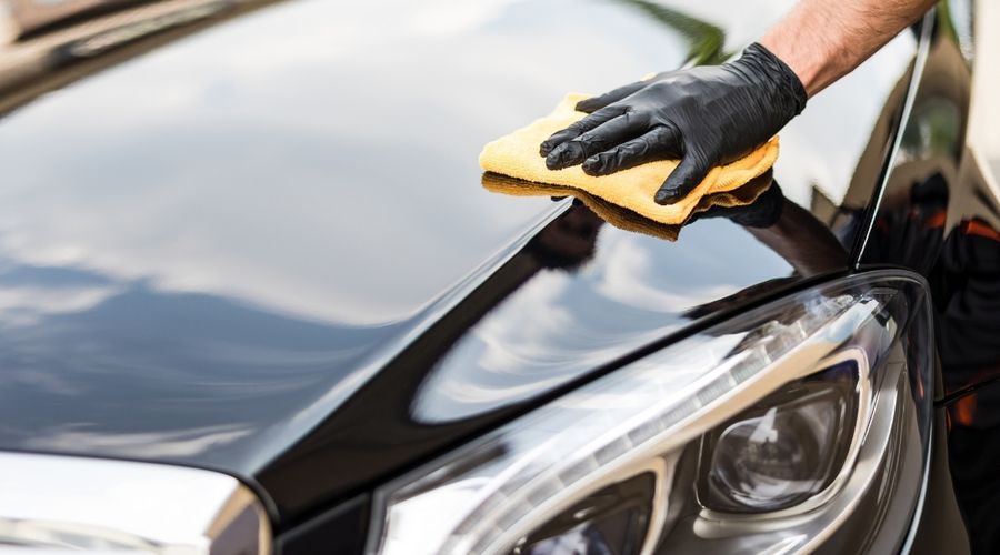 Mano aplicando cera a un capó negro brillante